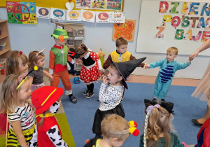 Dzieci tańczą w kole. W środku dziewczynka z czarnym kapeluszem