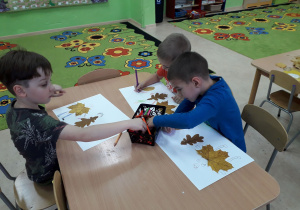 Dzieci przy stolikach wykonują pracę plastyczną z jesiennych liści.