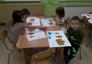 Dzieci przy stolikach wykonują pracę plastyczną z jesiennych liści.