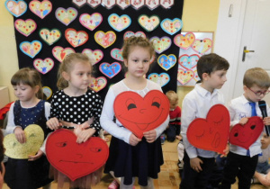 Dzieci trzymające duże czerwone serca i recytujące wiersze