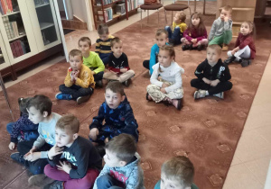 Dzieci siedzą na dywanie i oglądają prezentację multimedialną