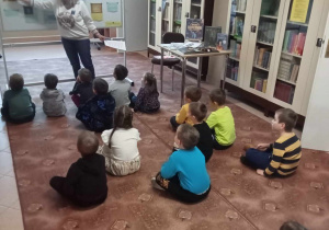 Dzieci siedzą na dywanie i słuchają pani bibliotekarki