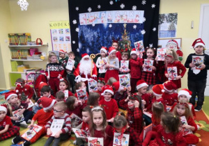 Dzieci trzymają prezenty i pozują do zdjęcia z Mikołajem.
