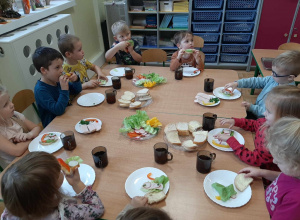 Dzieci z grupy 3,4,5 latków siedzą przy stole, na którym są zdrowe produkty. Przygotowują zdrowe i kolorowe kanapki.