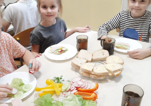 Grupa 5,6 latków. Dziewczynki siedzą przy stoliku, przygotowują zdrowe kanapki ze zdrowych produktów.