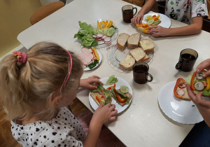 Grupa 5,6 latków. Dzieci przy stoliku przygotowują zdrowe kanapki, układają produkty tworząc ciekawe kompozycje.