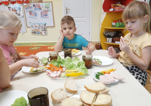 Grupa 5,6 latków. trójka dzieci przy stoliku podczas przygotowywania zdrowych kanapek.