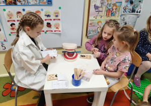 Scenka dramowa w grupie 5,6 latków. Dziewczynki siedzą przy stoliku, jedna z nich jest lekarzem i udziela konsultacji.