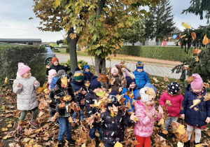 Dzieci z grupy 3,4,5 latków na powietrzu podczas zabawy ruchowej z liśćmi.