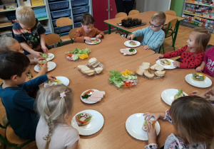 Dzieci z grupy 3,4,5 latków siedzą przy stole, na którym są zdrowe produkty. Przygotowują zdrowe i kolorowe kanapki, kolejne ujęcie.