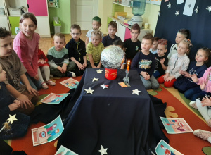 Przedszkolaki siedzą na dywanie wokół magicznego stolika, na którym stoi srebrna kula, świeci elektryczna świeczka.