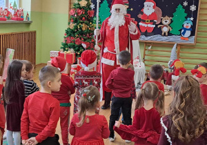 Dzieci stoją przed Mikołajem i śpiewają piosenkę