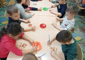 Dzieci z grupy 5-6 latków siedzą przy stoliku i malują ozdoby świąteczne.