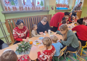 Dzieci i rodzice siedzą przy stole i dekorują pierniki
