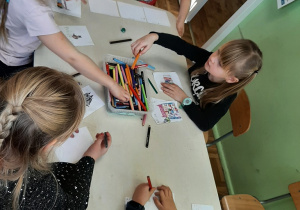 Kolejna grupa dzieci siedzi przy stoliku i rysuje na kartkach wymarzone prezenty.