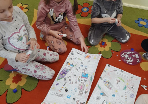 Kilka dziewczynek siedzi na dywanie dokleja kolorowe i błyszczące elementy ozdobne na list do Mikołaja - następne ujęcie.