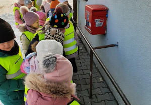 Dzieci przed budynkiem poczty w Wartkowicach, obserwują skrzynkę pocztową.