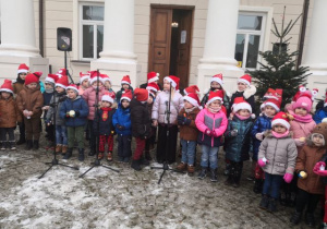 Przedszolaki w świątecznych czapkach śpiewają kolędy przed pałacem w Starym Gostkowie.