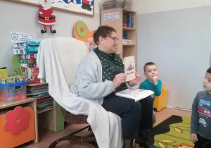 Pani bibliotekarka siedzi na fotelu i czyta dzieciom bajkę