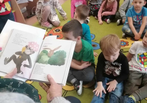Dzieci siedzą na dywanie przed panią z książką
