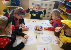 Dzieci siedzą przy stoliku i kolorują obrazki.