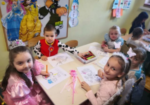 Dzieci siedzą przy stoliku i kolorują obrazki.