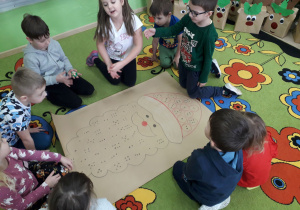 Dzieci na dywanie w sali bawią się z kostką i sylwetą Mikołaja.