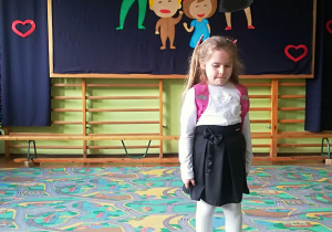 Dziewczynka w stroju przedszkolaka na tle dekoracji.