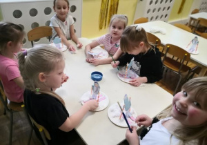 Dzieci siedzą przy stoliku i wykonują pracę plastyczno-techniczną.