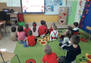 Dzieci siedząc na dywanie oglądają film edukacyjny "Legenda o Św. Walentym".