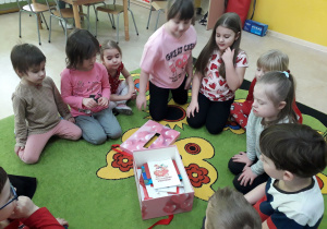 Dzieci na dywanie oglądają zawartość skrzynki walentynkowej.