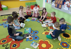 Dzieci na dywanie prezentują swoje ulubione książeczki z bajkami.