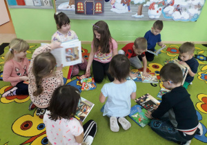 Dzieci na dywanie prezentują swoje ulubione książeczki z bajkami.
