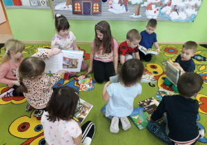 Dzieci na dywanie wymieniają się swoimi książeczkami z bajkami.