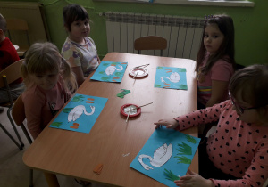 Dzieci przy stolikach wykonują pracę plastyczną "Brzydkie kaczątko".