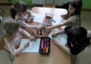 Dzieci przy stolikach kolorują głowę smoka.