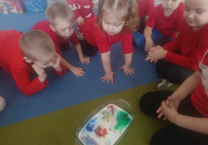 Dzieci siedzą na dywanie i oglądają eksperyment z mlekiem