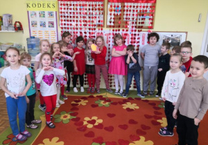 Przedszkolaki pozują do zdjęcia, na dywanie ułożone jest przez dzieci duże serce z serduszek.