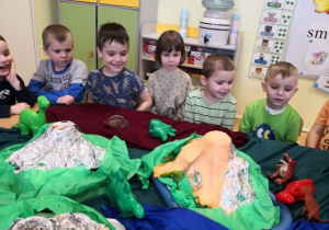 Dzieci siedzą przy stoliku i obserwują eksperyment "wybuch wulkanu".