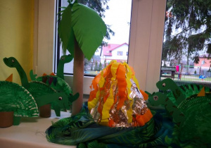 Wystawa prac dzieci przedstawiająca dinozaury i wulkan.