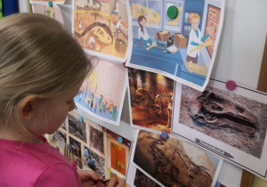 Dziewczynka ogląda na tablicy obrazki przedstawiające pracę paleontologa.