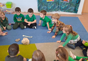 Dzieci siedzą na dywanie i oglądają skamieniałości i kości