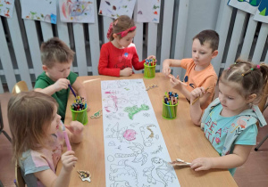 Dzieci podczas kolorowania plakatu z dinozaurami siedzą przy stolikach