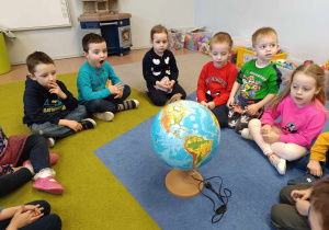Dzieci siedzą na dywanie na którym stoi globus