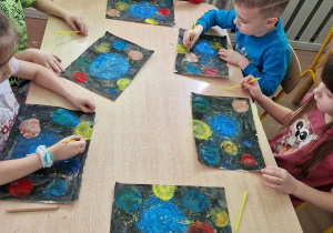 Dzieci przy stolikach wykonują pracę plastyczną z planetami