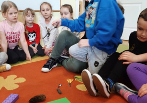 Dzieci siedzą na dywanie. Chłopiec za pomocą magnesu przyciągnął metalową łyżkę.