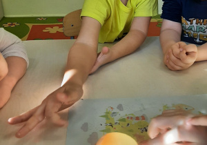 Dzieci przy stoliku sprawdzają jak zmieniła się skorupa jajka pod wpływem octu, badają jej "gumową" strukturę.
