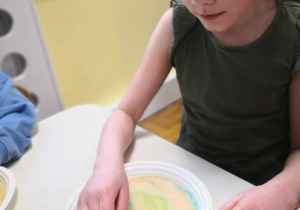 Malowanie na mleku. Kolejna dziewczynka tworzy na mleku z barwnikami kolorowe wzory z użyciem płynu do naczyń.