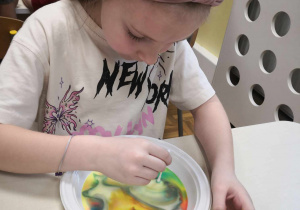Malowanie na mleku. Dziewczynka tworzy na mleku z barwnikami kolorowe wzory z użyciem płynu do naczyń.