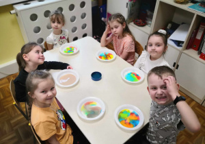 Malowanie na mleku. Dzieci przy stoliku prezentują na kolorowe wzory namalowane na mleku.